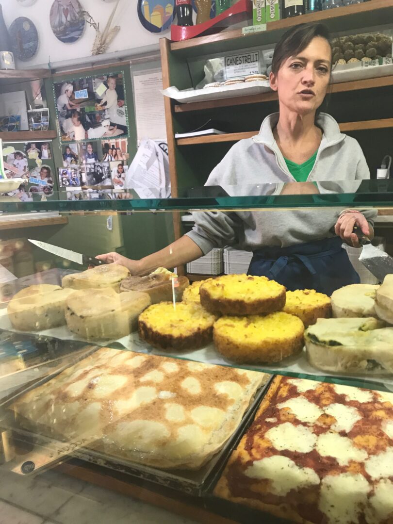 A woman sitting behind a counter with many different types of food.